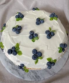 a white frosted cake topped with blueberries and green leaves on top of a table