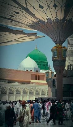 many people are walking around in front of a green and white dome building with gold accents