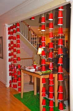 a room filled with lots of red cups on top of a wooden table next to a stair case