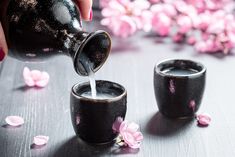 a person pouring water into two black cups