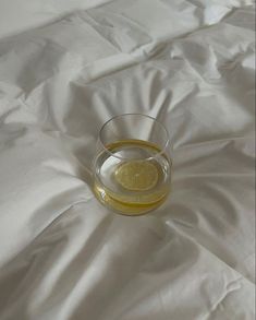 a glass filled with liquid sitting on top of a white bed cover covered in sheets