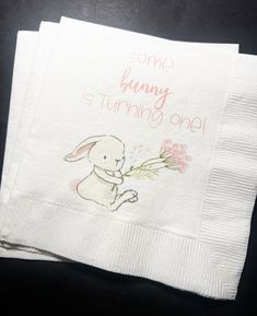 some bunny is turning one napkins on top of each other with pink flowers and the words, some bunny is turning one