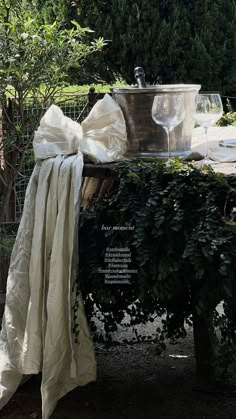 a table covered in white cloth next to a potted plant and glassware on top of it