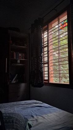 a bed sitting under a window next to a book shelf