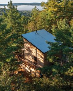 a small cabin nestled in the woods on top of a hill with trees around it