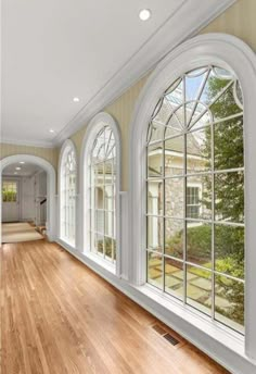 an empty room with large windows and hardwood floors in front of the window is a hallway leading to another room