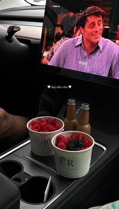 two cups of ice cream and raspberries in front of a tv screen on a car console