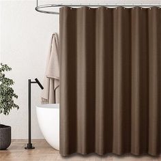 a brown shower curtain in a bathroom next to a white bathtub and potted plant