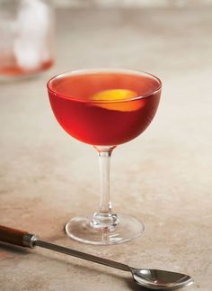 a glass filled with red liquid next to a spoon