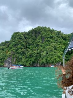 a woman on a boat in the water looking out at some green hills and trees