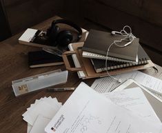 a pile of papers and headphones on top of a wooden table next to a laptop