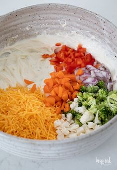 a bowl filled with cheese, broccoli and carrots next to other vegetables