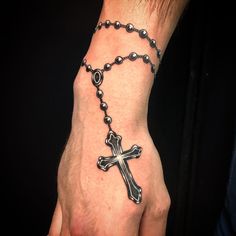 a hand with a rosary and a cross tattoo on it's left wrist is shown