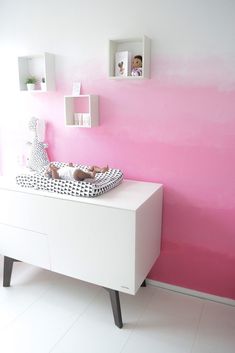 a baby's crib in front of a pink and white wall with shelves