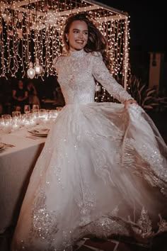 a woman in a white dress standing next to a table covered with candles and lights