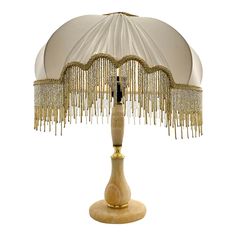 a white lamp with gold fringes on it's base and a beige shade