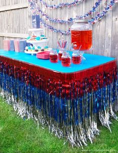 a table with red, white and blue decorations on it in the grass near a fence