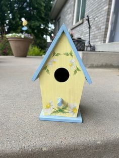 a yellow birdhouse with flowers painted on it's side sitting in front of a house