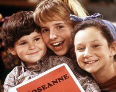 two girls and a boy are smiling while holding a book in front of their face