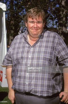 a man standing in the grass with his hands in his pockets and smiling at the camera