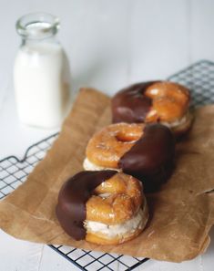 chocolate covered donuts sitting on top of a brown paper bag next to a glass of milk