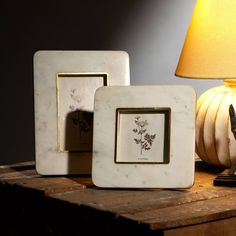 three white marble photo frames sitting on top of a wooden table next to a lamp