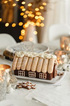 a gingerbread house with icing on it sitting on a table next to candles