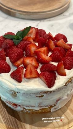 a cake with white frosting and strawberries on top sitting on a wooden platter