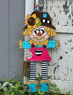 a door hanger with a cartoon doll on it's face and legs, standing in front of a wooden door