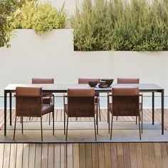 a table and chairs on a wooden deck next to a swimming pool with plants in the background