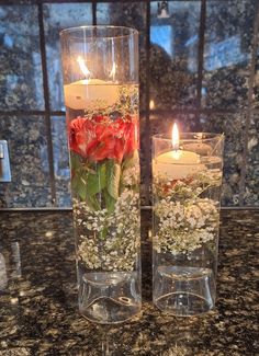 two vases filled with flowers and candles on a counter