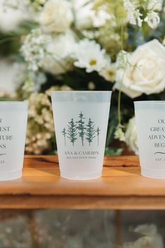 three shot glasses sitting on top of a wooden table next to white flowers and greenery