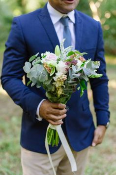 a man in a blue suit holding a bouquet of flowers and greenery on his lapel