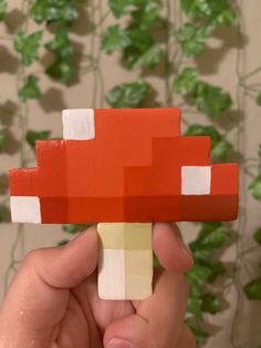 a hand holding up a piece of paper that looks like a mushroom with red and white squares on it