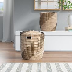 two woven baskets sitting on top of a wooden floor next to a white vase and potted plant