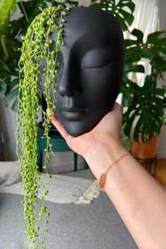 a person holding up a black mask with green plants growing out of it