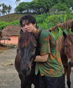 a young man is hugging his horse on the street in front of some huts and trees