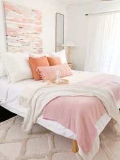 a bed with pink and white pillows on top of it in a bedroom next to a window