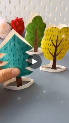 someone is holding an origami christmas tree in front of some other paper trees