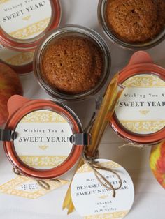 four jars with labels on them sitting next to an apple and some other food items