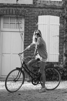 black and white photograph of woman on bicycle with dog in front of brick building, outdoors