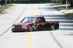 a red truck with flames painted on it's side driving down the road in front of trees