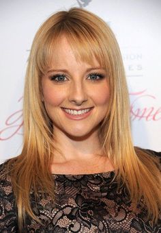 a woman with long blonde hair and blue eyes smiles at the camera while standing in front of a red carpet