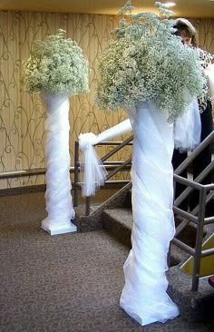 two tall white vases with flowers and tulle are on the stairs at a wedding