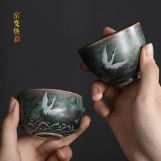 two hands holding small bowls with white birds painted on the sides and green paint on the outside