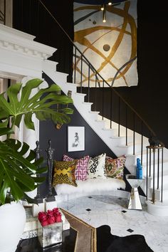 a living room filled with furniture and a stair case next to a white couch covered in pillows