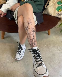 a woman sitting on a chair with her legs crossed and flowers tattooed on the leg