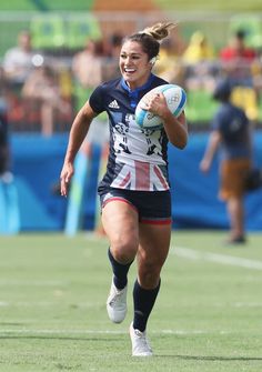 a woman running with a rugby ball in her hand and people watching from the stands