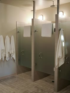 three white towels hanging on the wall next to two glass partitions in a bathroom