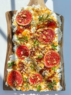 a pizza topped with cheese and tomatoes on top of a wooden cutting board next to a white wall